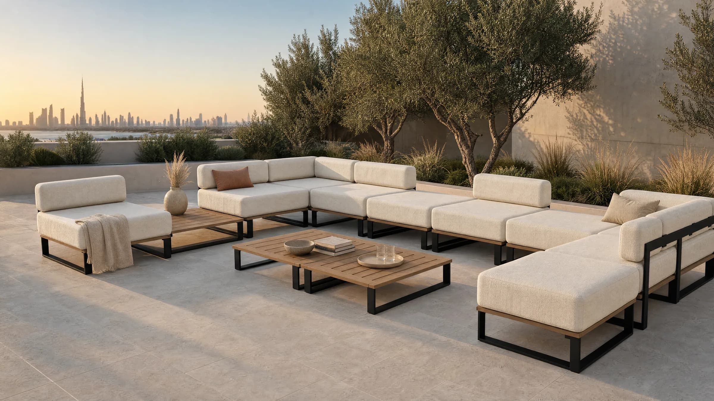 A Nour arrangement on a Dubai terrace in the late afternoon: separate 800 millimetre modules standing flush along three sides of an open centre, two slatted teak tables in the middle, olive trees and dry grasses against a limewashed wall, and the city on the horizon beyond.