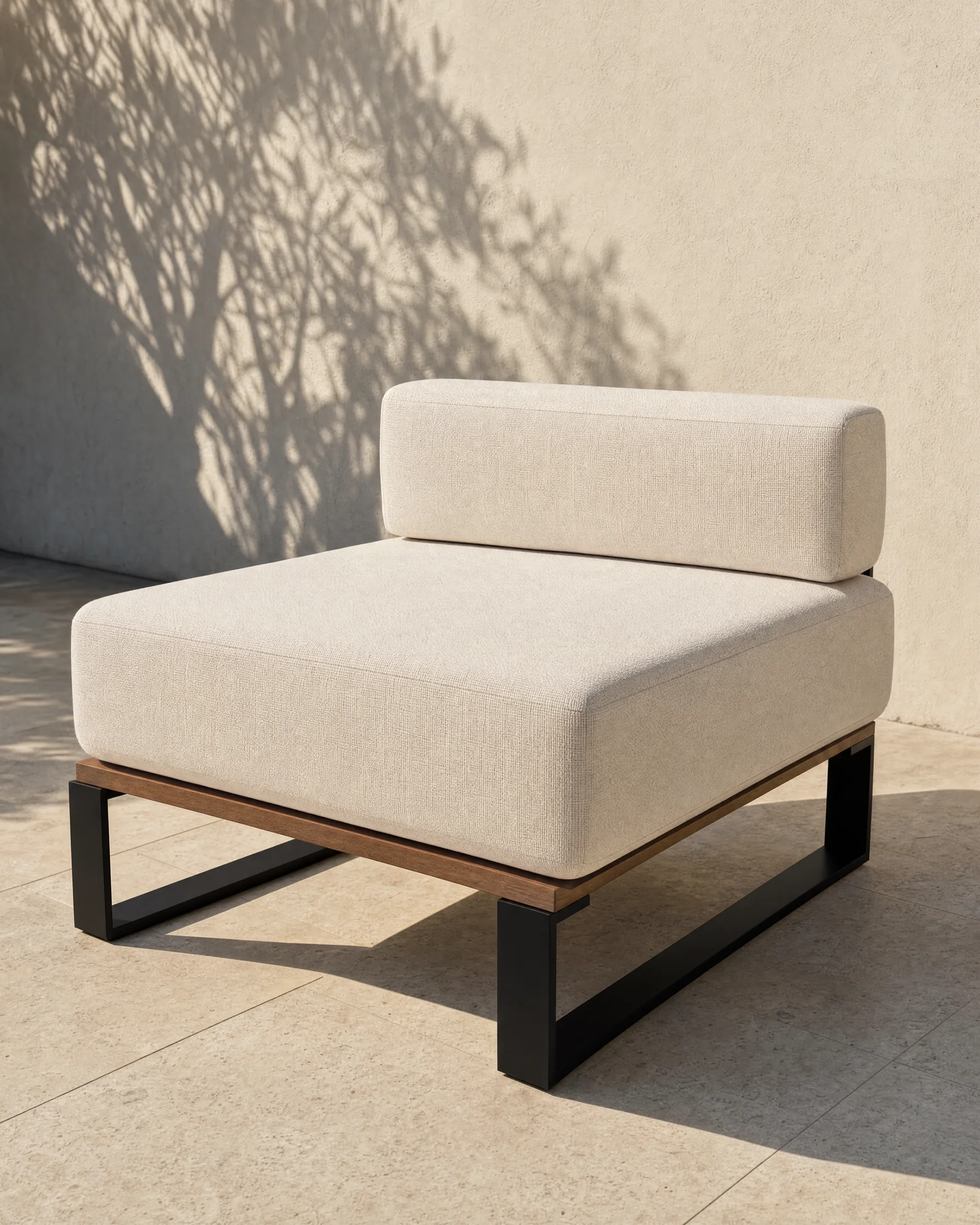 The Nour centre module alone on a terrace: an 800 millimetre square seat with a single back bolster, on a matte black frame over an oiled teak rail, against a limewashed wall with the shadow of olive leaves across it.