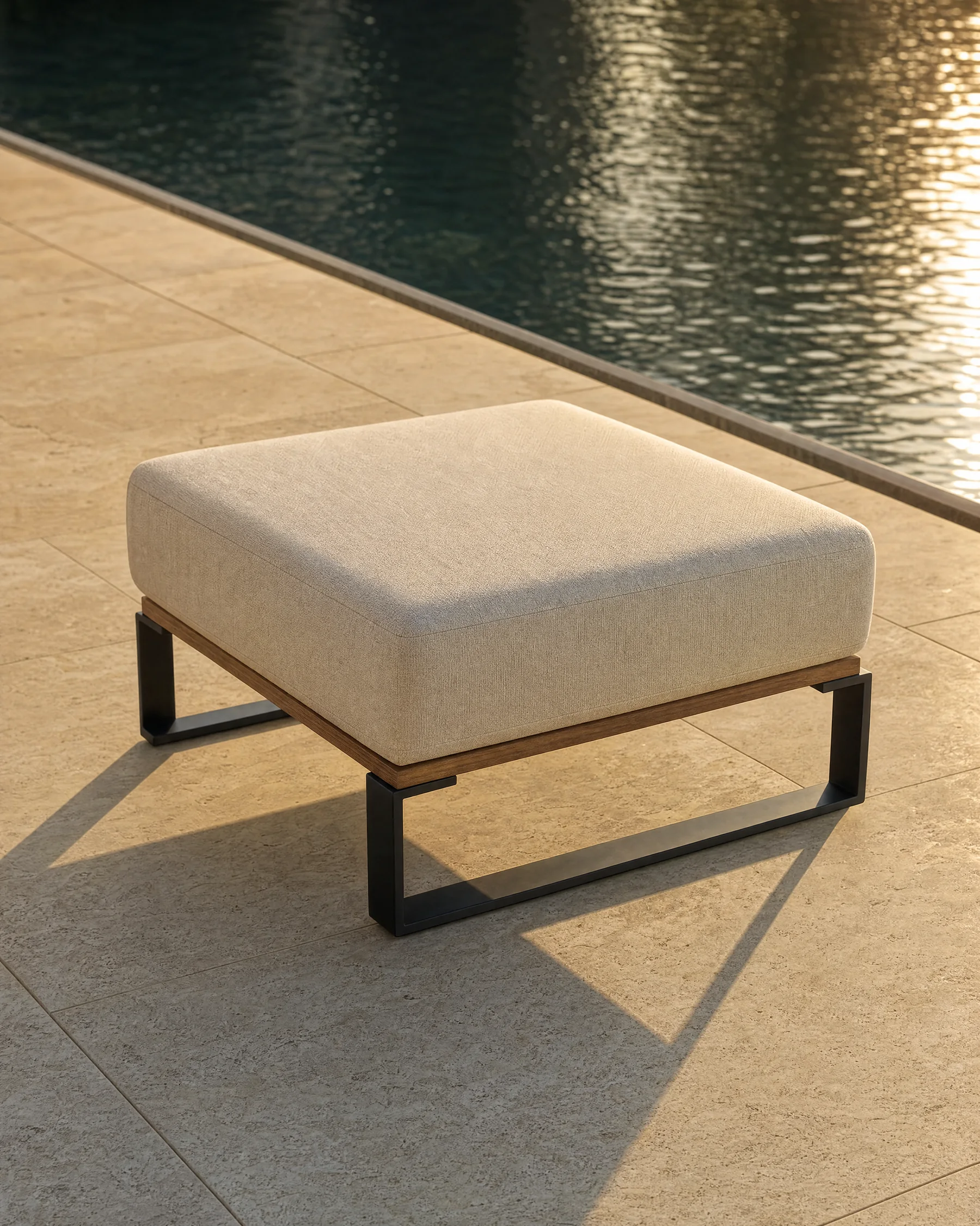 The Nour pouf alone beside a dark reflecting pool: an 800 millimetre square seat with no back at all, on a matte black frame over an oiled teak rail.