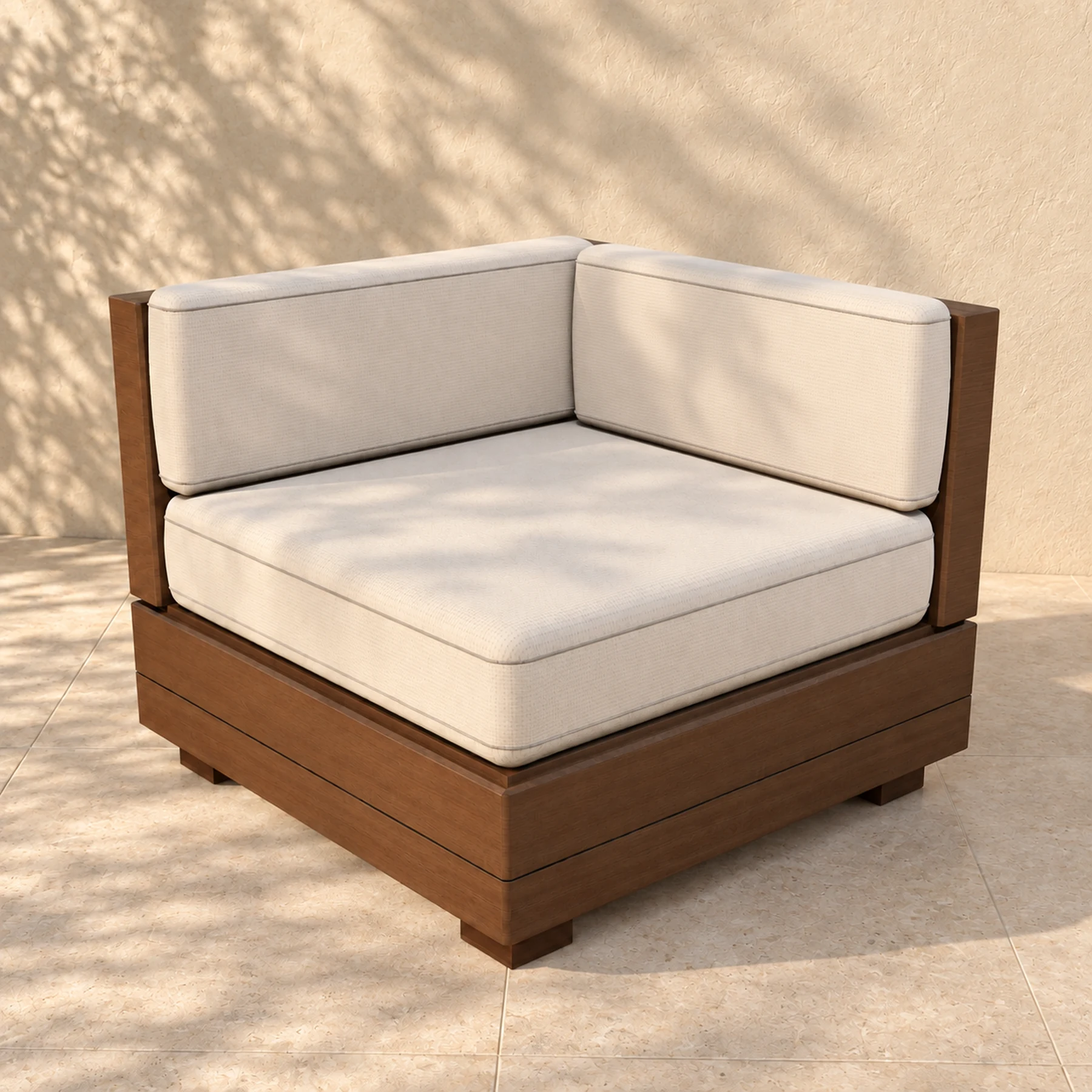 The Sama corner module alone on pale limestone paving before a warm plaster wall, the shadow of an olive tree across it: two timber back boards meeting in a mitre at the corner of an 800 millimetre square plinth, with a boxed cushion against each.