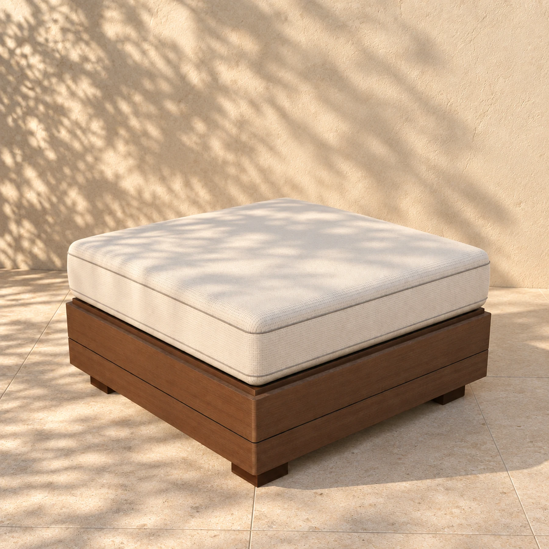 The Sama pouf alone on pale limestone paving before a warm plaster wall, the shadow of an olive tree across it: an 800 millimetre square boxed cushion on a closed timber plinth, no back and no arms.