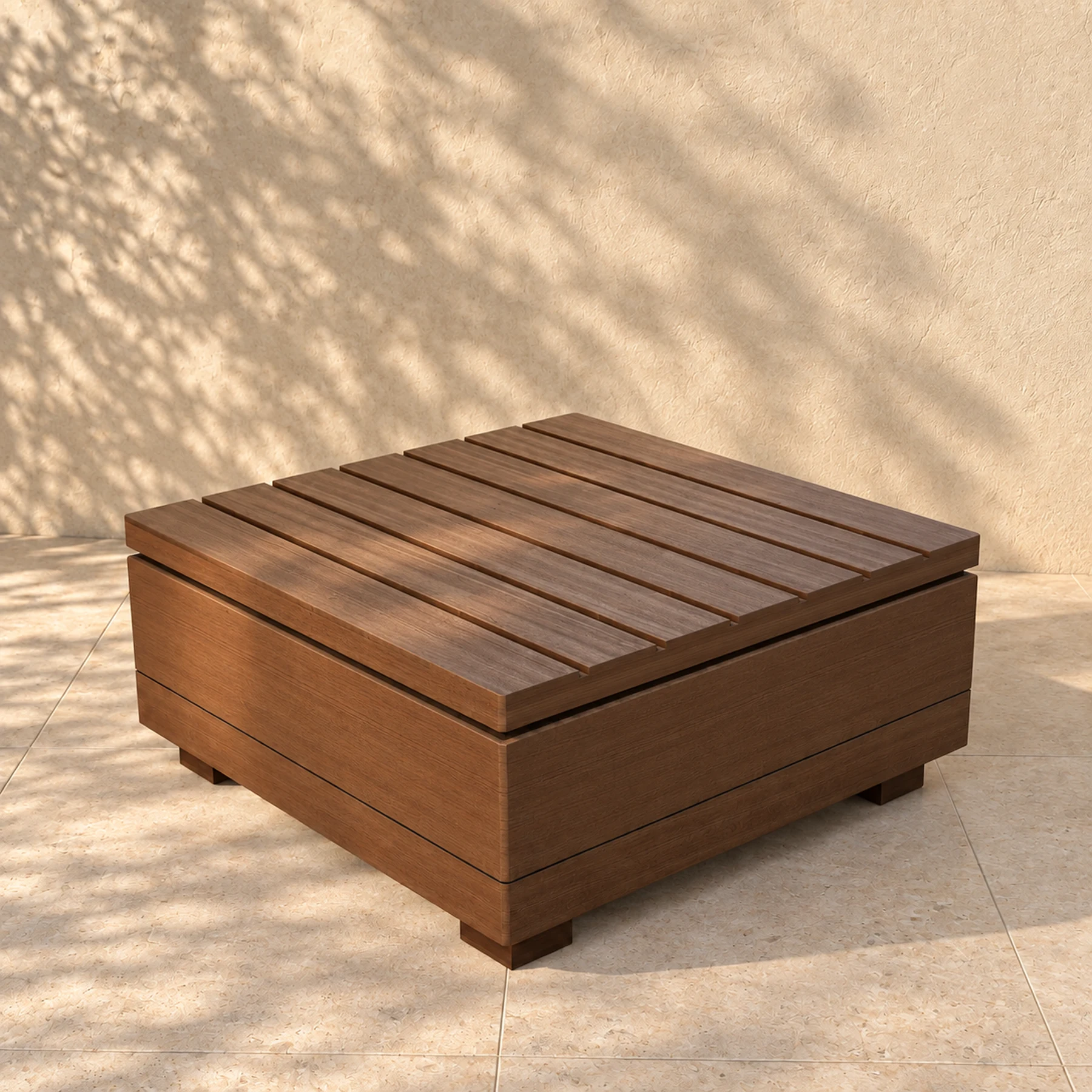 The Sama low table alone on pale limestone paving before a warm plaster wall, the shadow of an olive tree across it: a slatted solid timber top on the same square plinth as the seating, standing clear of the floor on four short timber feet.