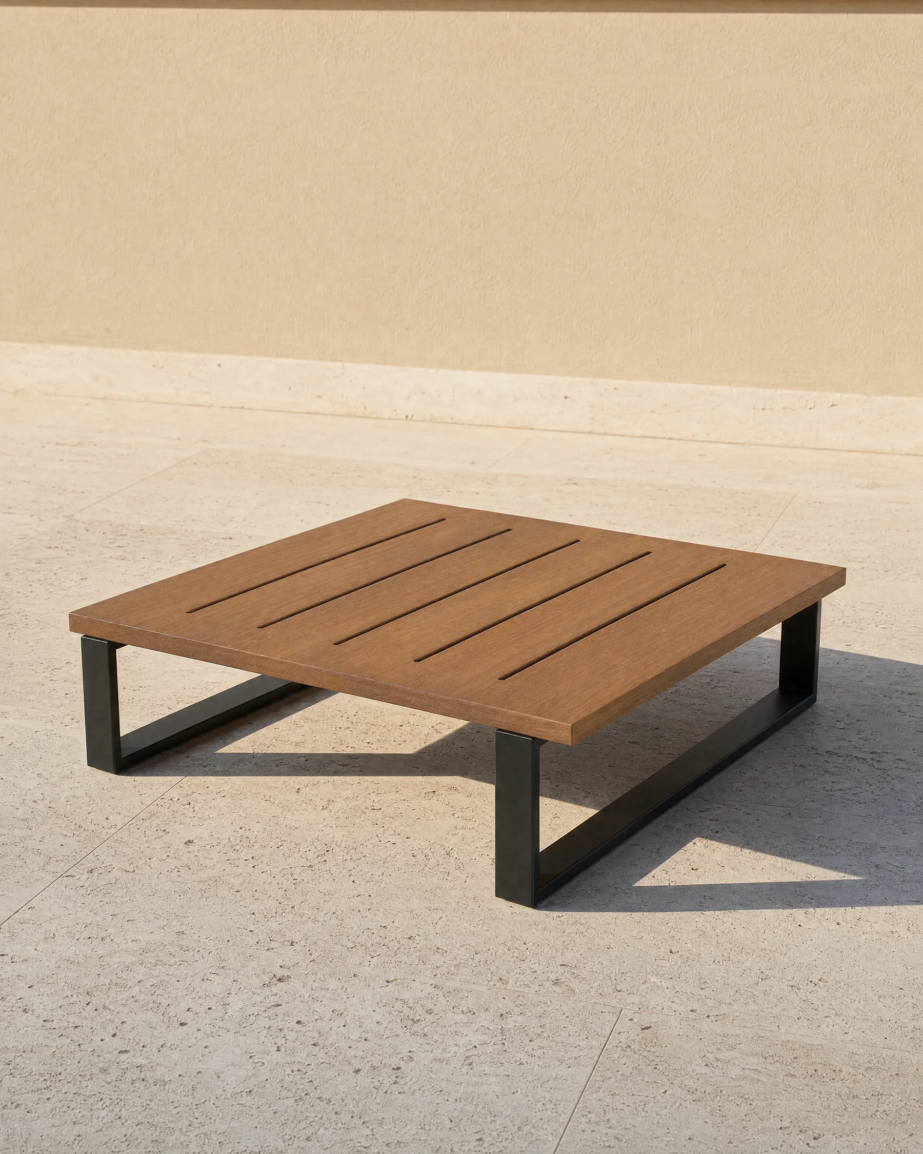 The Nour coffee table alone on travertine paving: an 800 millimetre square top of seven oiled teak slats, 200 millimetres high, on a matte black frame.
