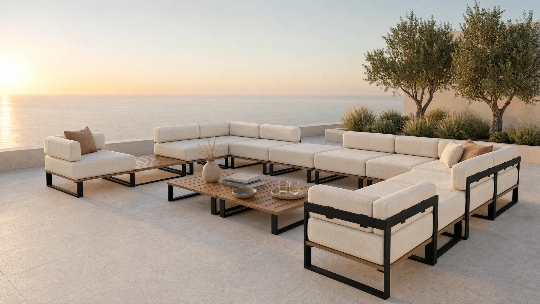 A Nour arrangement on a terrace above the sea in the middle of the day: a U of modules round two low tables, with a flat blue horizon beyond the parapet.